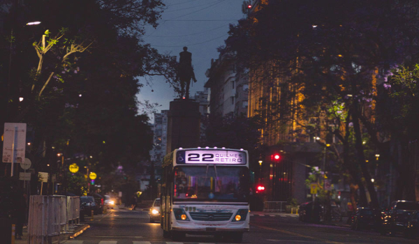 A photograph of a bus traversing a crowded city street at dusk