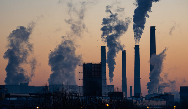 A photograph of an industrial park at dusk, smoke belching from tall stacks