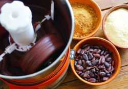 A photograph of a coffee grinder with beans and tumeric on the table