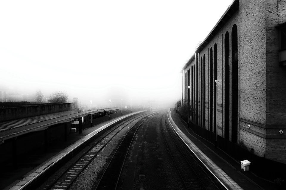 A black and white photo of train tracks stretching into a high-contrast distance