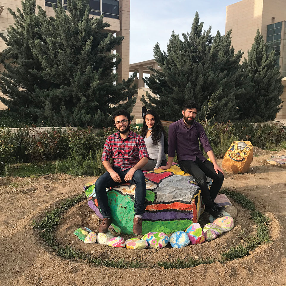 Three students pose on the painted rocks in the garden at Kashkul