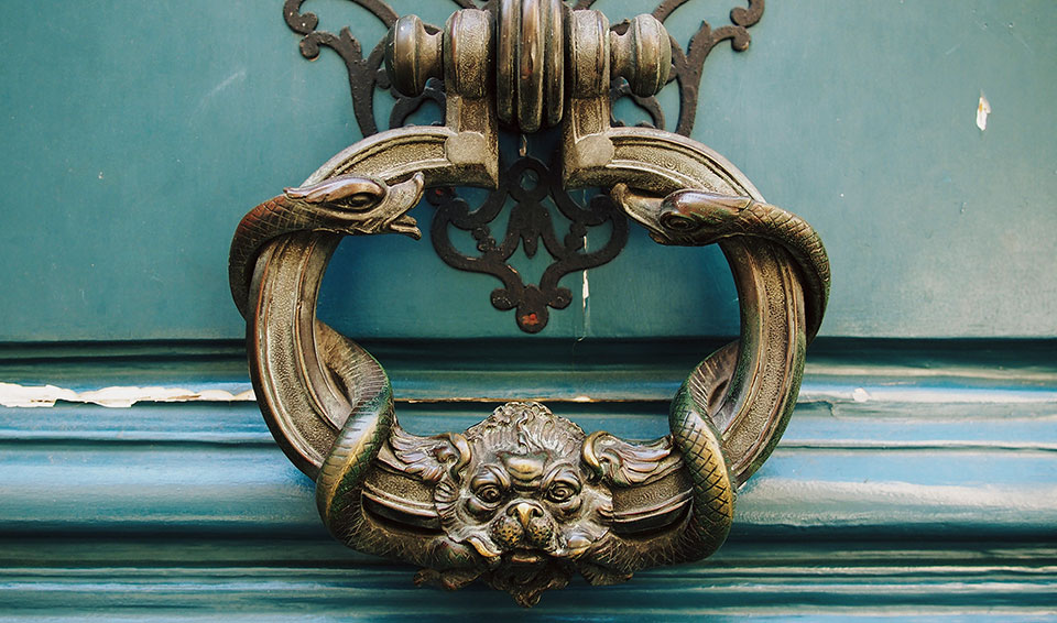 An ornate brass door knocker rests on a dark turquoise door