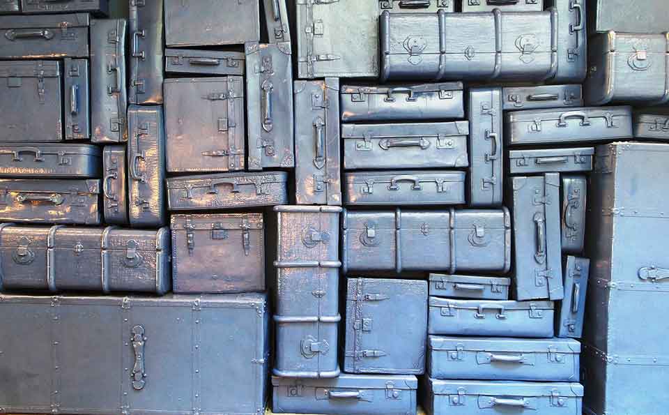 Many pieces of luggage, all spray painted uniformly with a metallic sheen, stacked into a wall