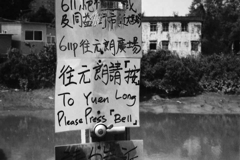 A hand-lettered sign in Chinese with English words that read “To Yuen Long / Please Ring Bell”