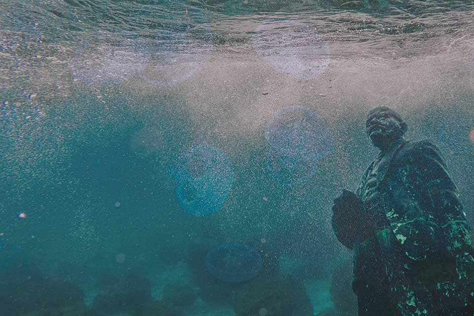 An underwater photo with a decaying statue of Lenin at the extreme right of the frame