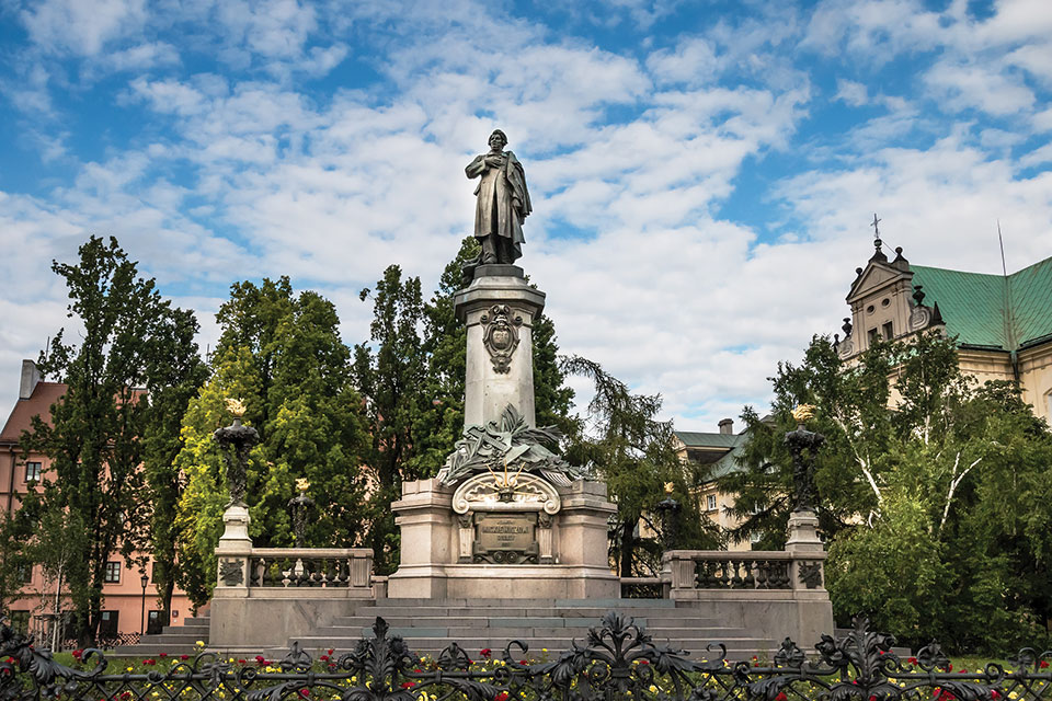 A monument to poet Adam Mickiewicz, surrounded by trees under a blue sky dotted with clouds