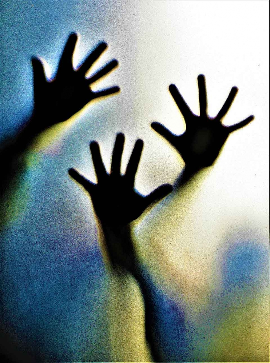 A photograph of hands pressed up against material, backlit by blue and yellow light
