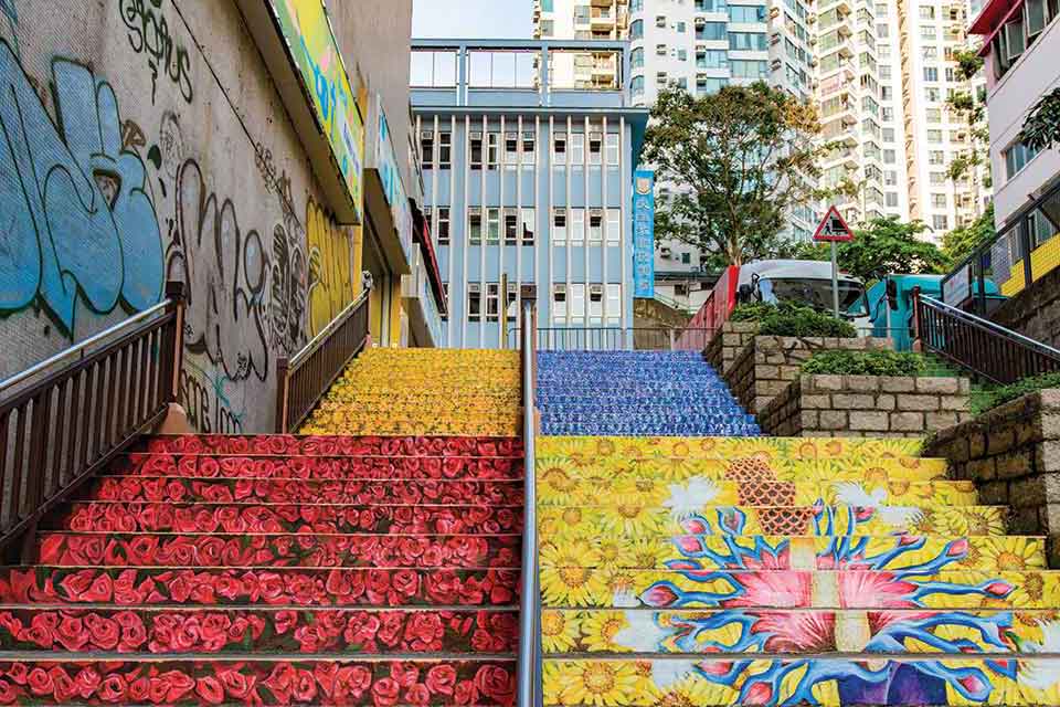 A long flight of stairs in a crowded city. The stairs are painted with red and yellow flowers. 