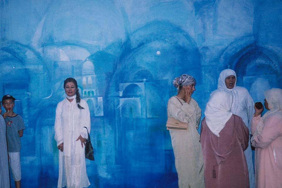 A photograph of people in Arab dress standing in front of a mural of a landscape in blue