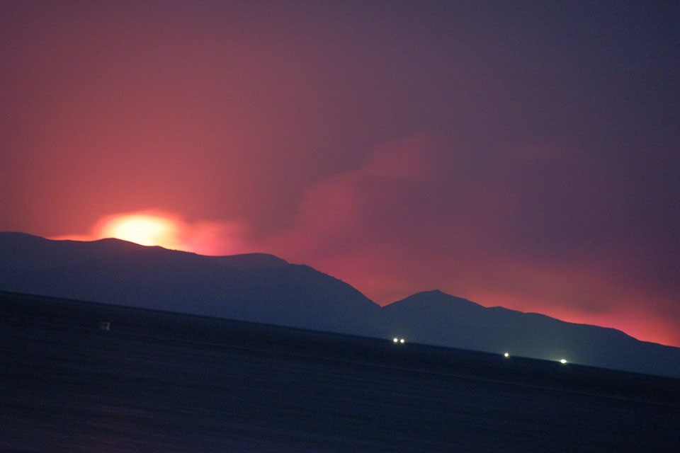 A photograph of a landscape at night, a fire burning ominously behind a hill in the background
