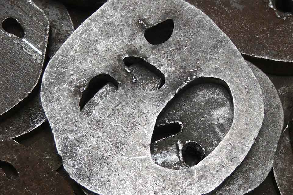 A photograph of a metal fittings with holes cut into them that resemble human faces