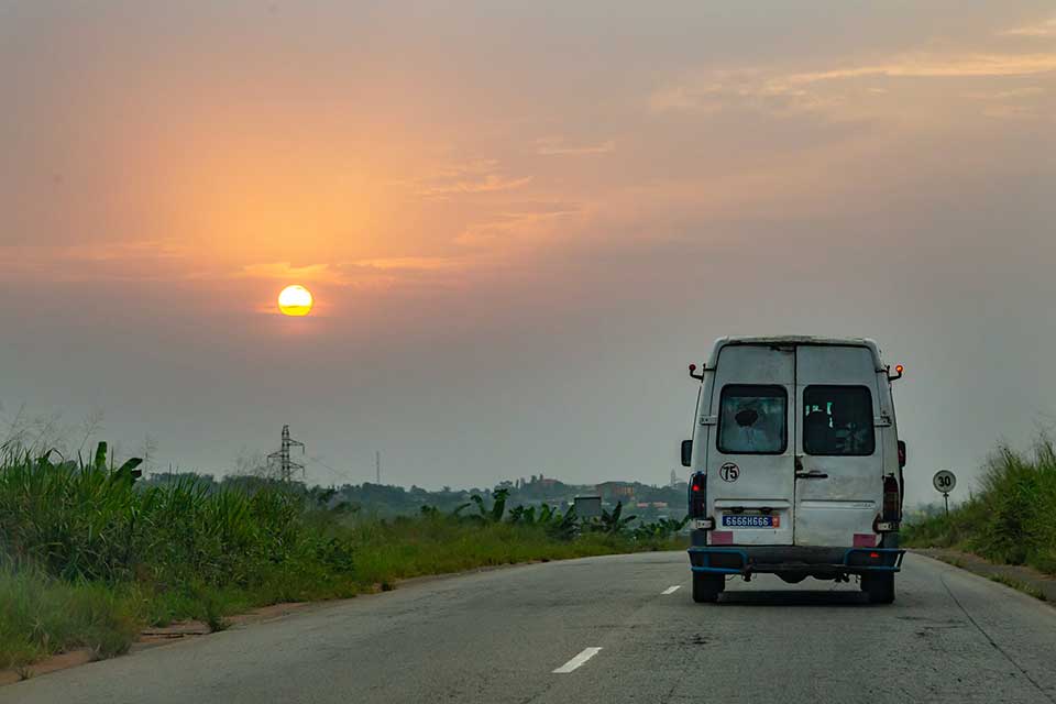 A photograph from behind of a van driving away into the sunset