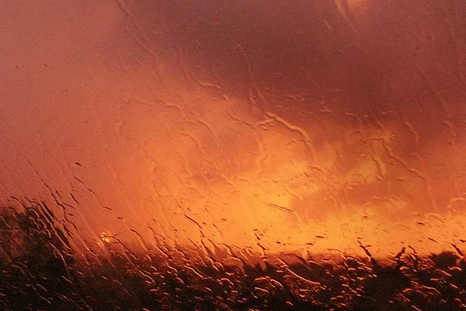 A photograph of a orange hued landscape as seen through a rain-swept window