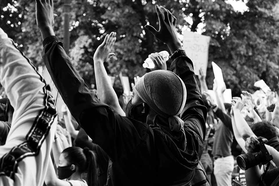 A black and white photo of a masked protestor with his hands up