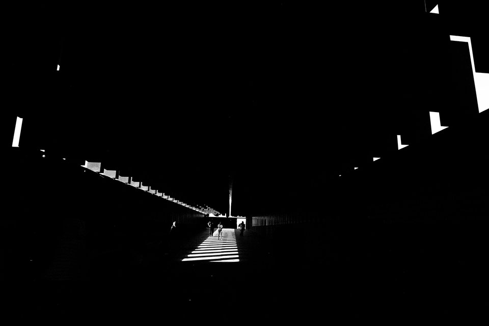 A photograph of the interior of the The National Memorial for Peace and Justice, mostly swallowed in darkness with a small path lit in the center and small slits visible on the walls