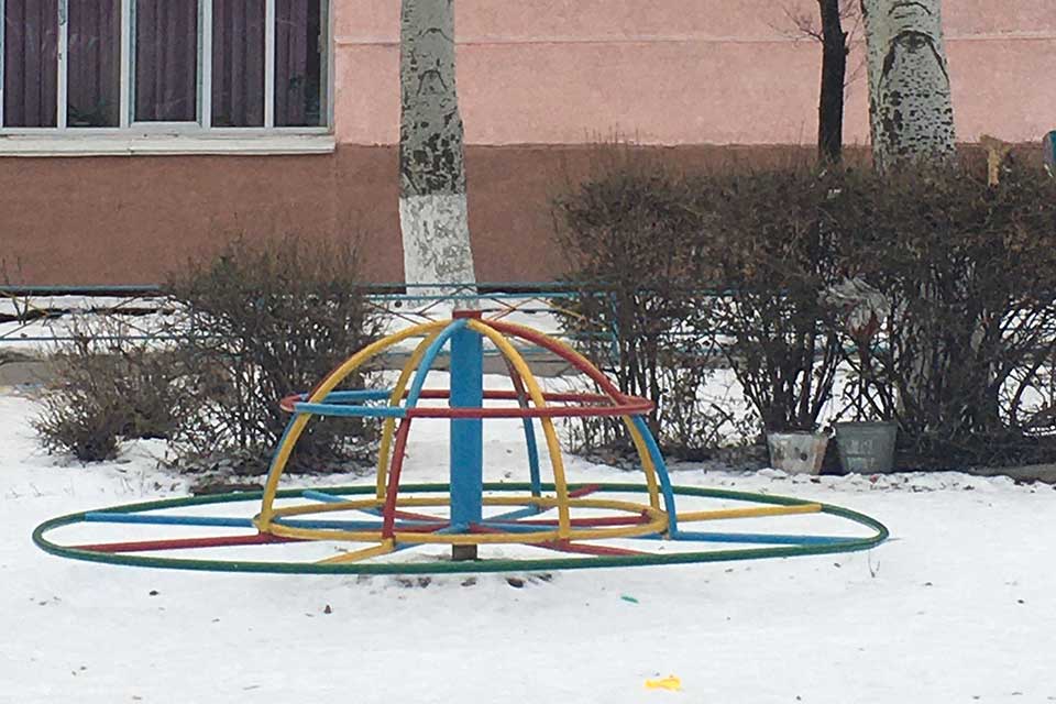 A photograph of a multi-colored merry go round on the snowy ground outside of a school