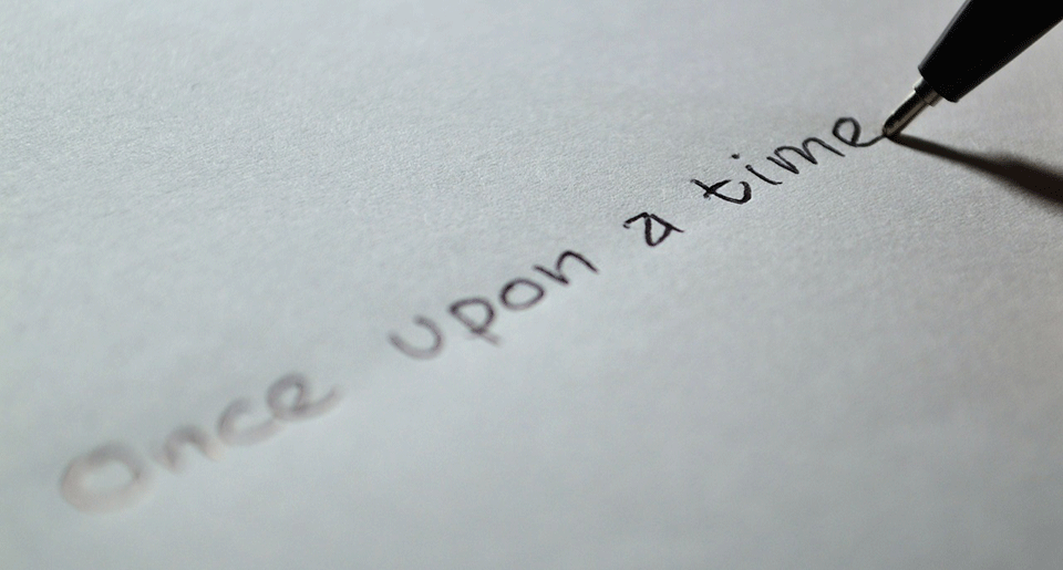 The words "Once upon a time" written on a piece of paper with a ink pen resting but poised to continue on the final stroke