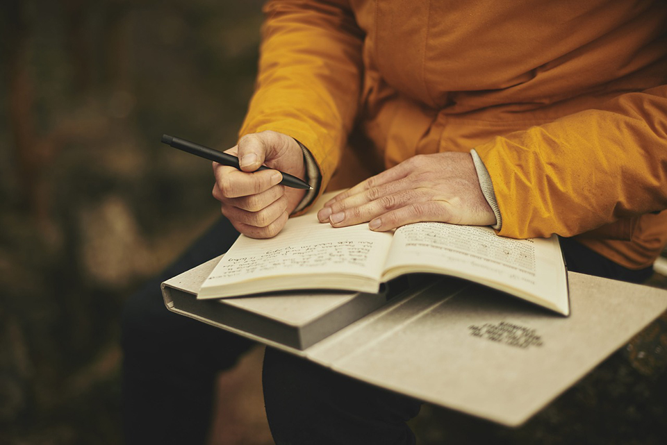 Person in a golden yellow jacket writing in a notebook.