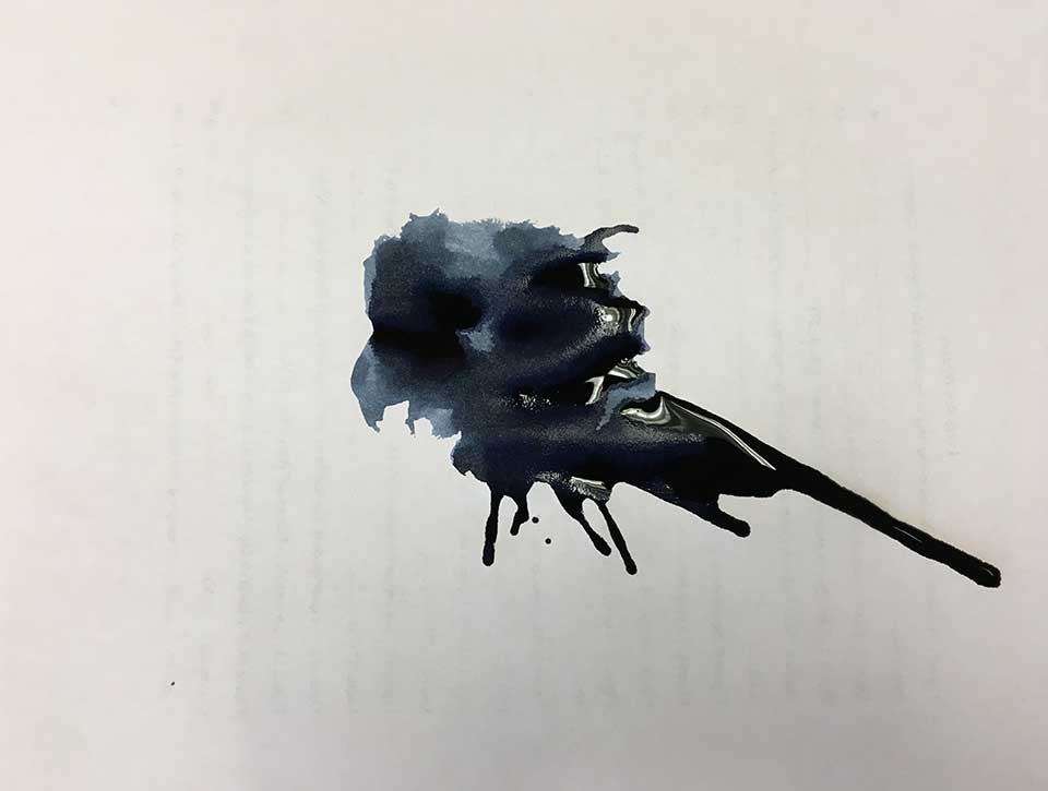 A large inkblot stain on white paper, through which writing on the opposite side just just be seen but not read