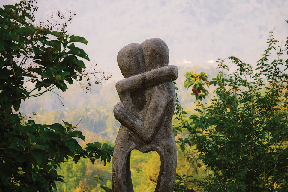 A photograph of a stone sculpture of two humanoid figures embracing. The status is in a jungle