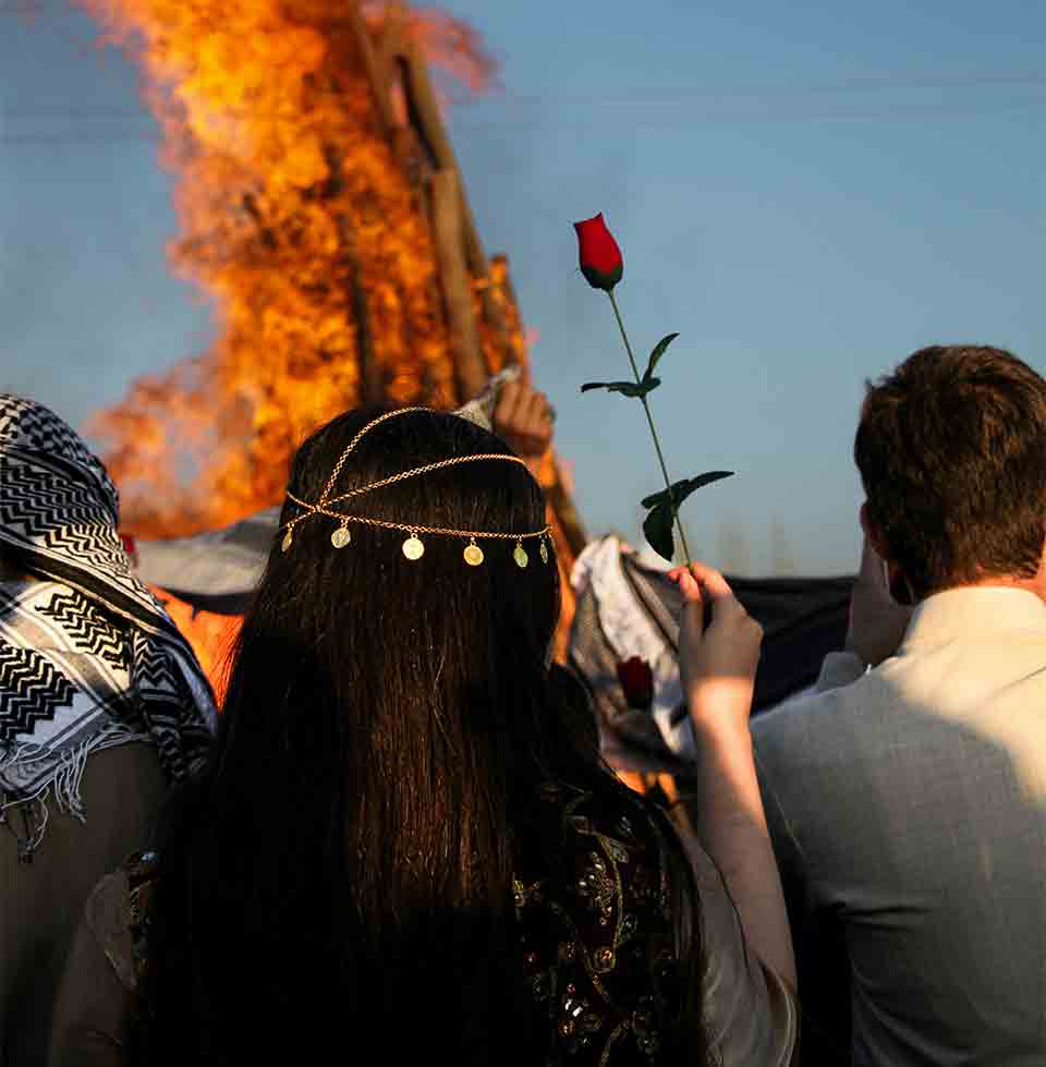 Protestor holds up a rose as a crowd watches something burn