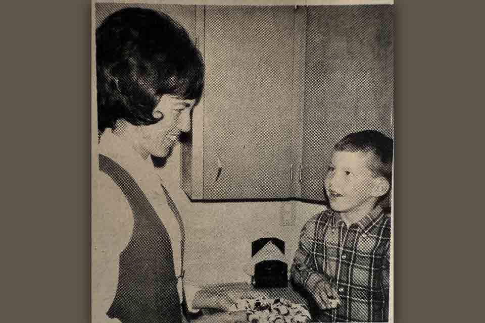 An aged newspaper photograph of an adult woman smiling at a small boy