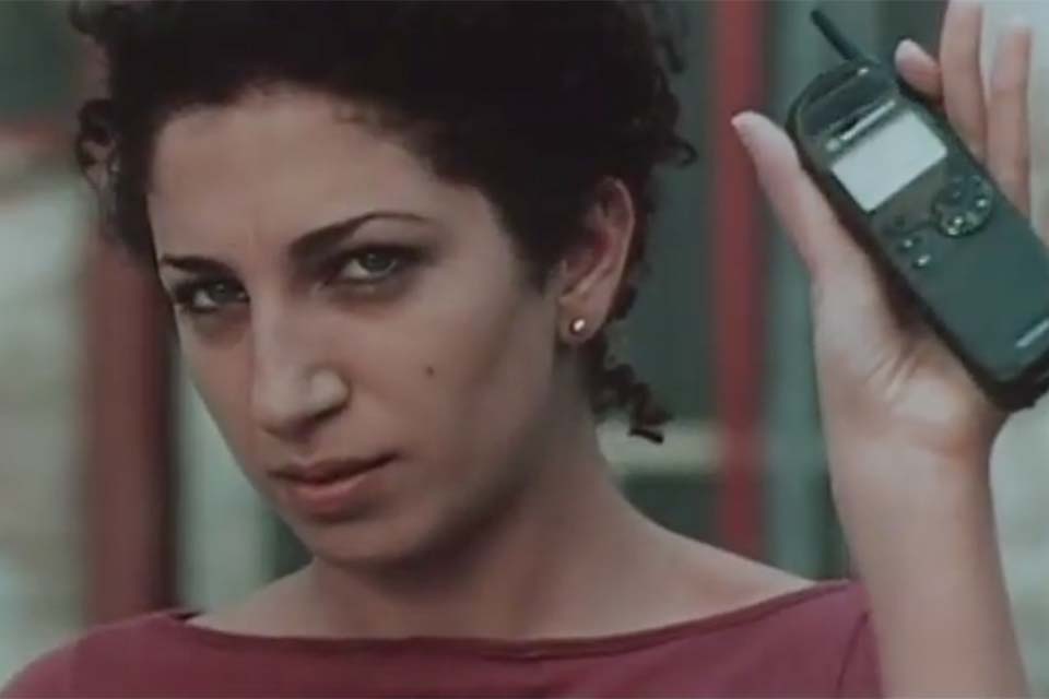 A woman looks at the viewer while holding up a cell phone