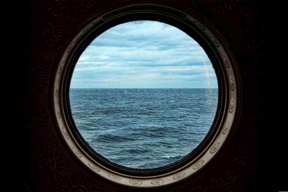 A photograph of a porthole window on a ship, looking out at the ocean