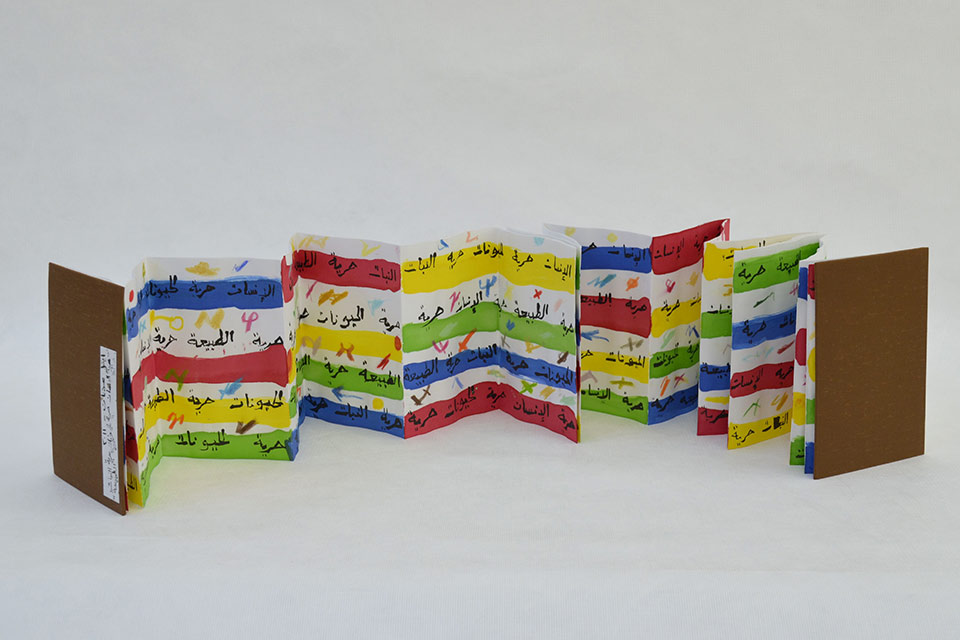 A photograph of an unfolded book with Arabic writing inside of it, offset by colored bands