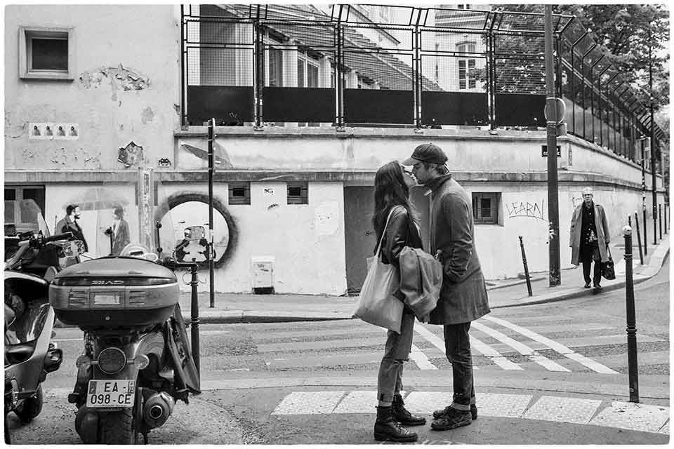 A black and white photograph of a man and a woman kissing in on a busy city street