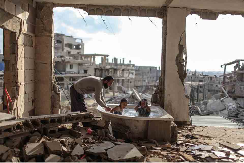 A man bathes two children in the rubble of a bombed-out apartment