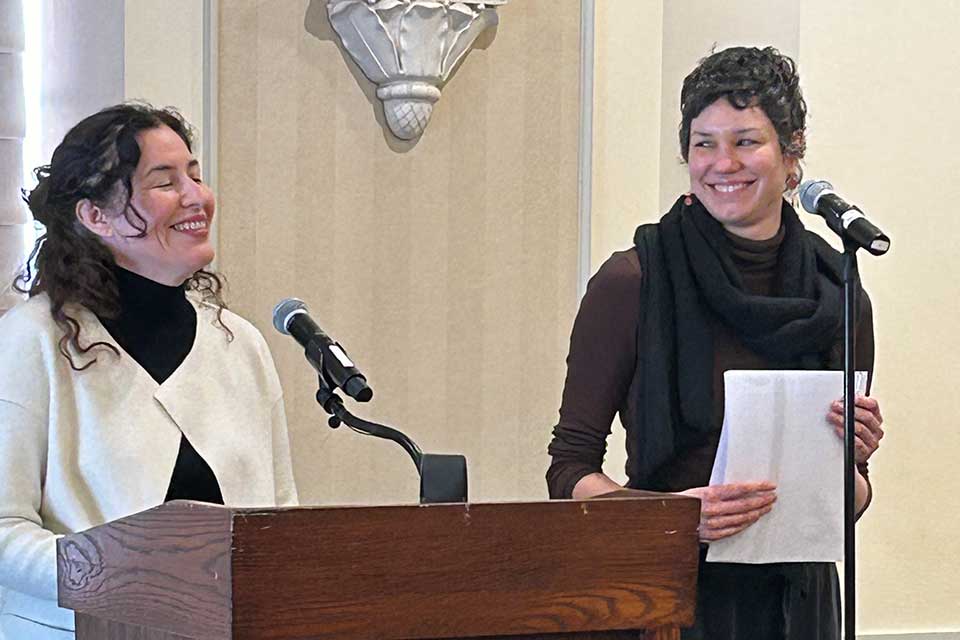 Guadalupe Nettel stands at the lectern laughing while Rosalind Harvey watches her, smiling