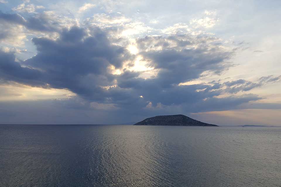 An island, shrouded in darkness, a light can be seen on the sea surrounding peeking in from the edges
