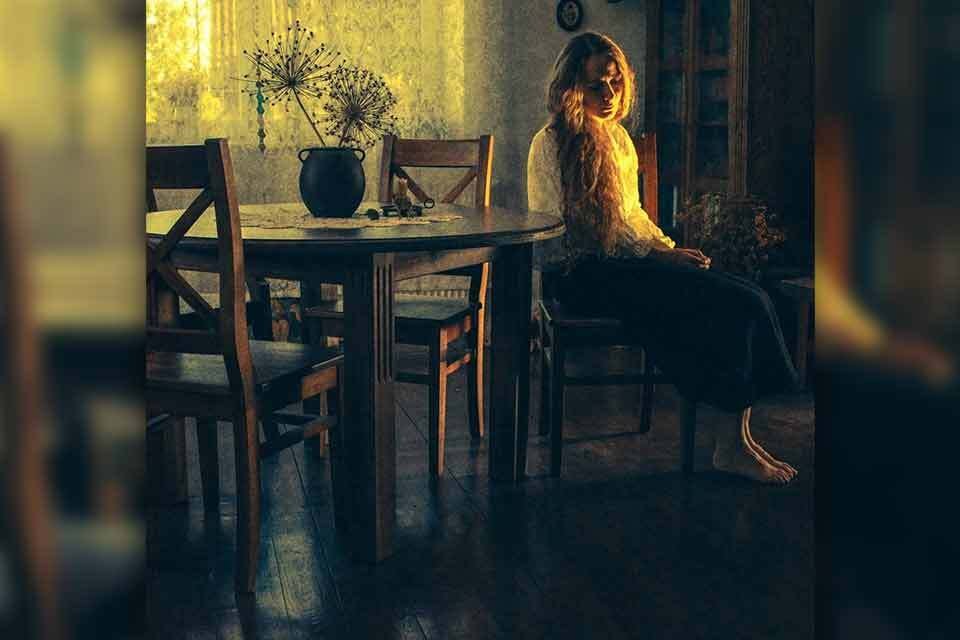 A woman sits in a chair looking at the floor with melancholy