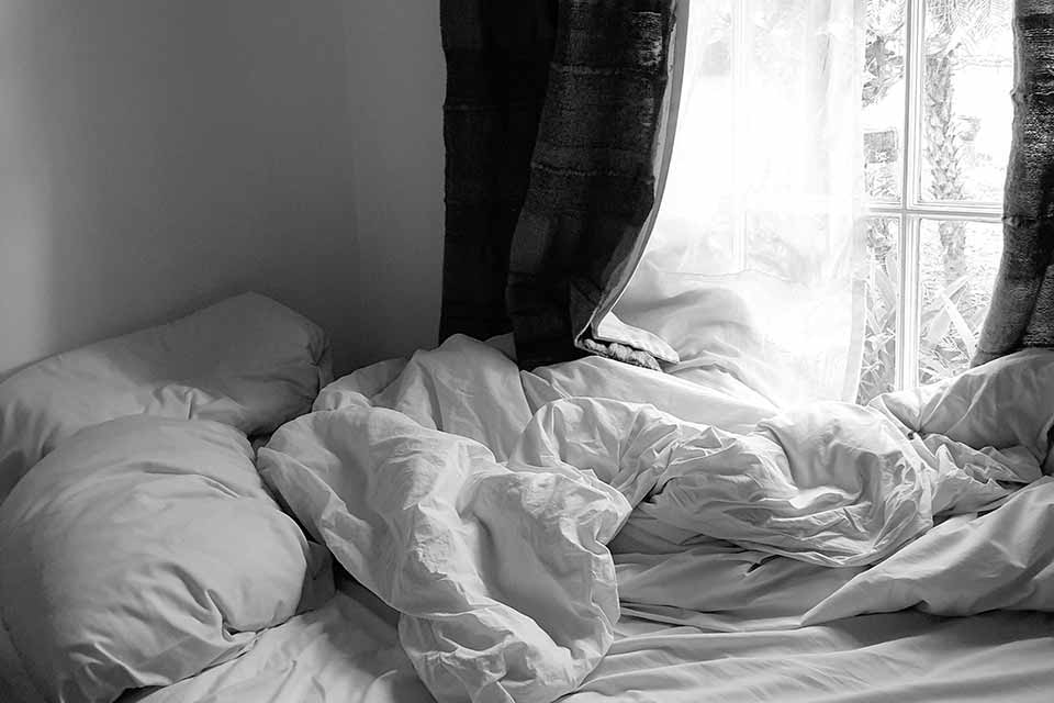 An unamde bed, bathed in light from a nearby window