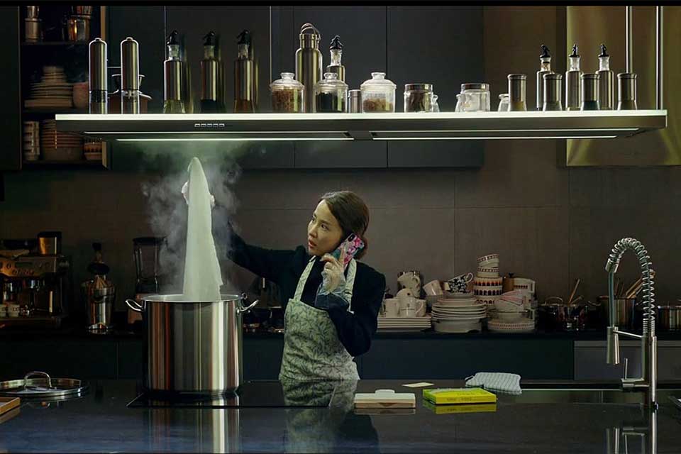 A woman stands in a shadowy kitchen cooking