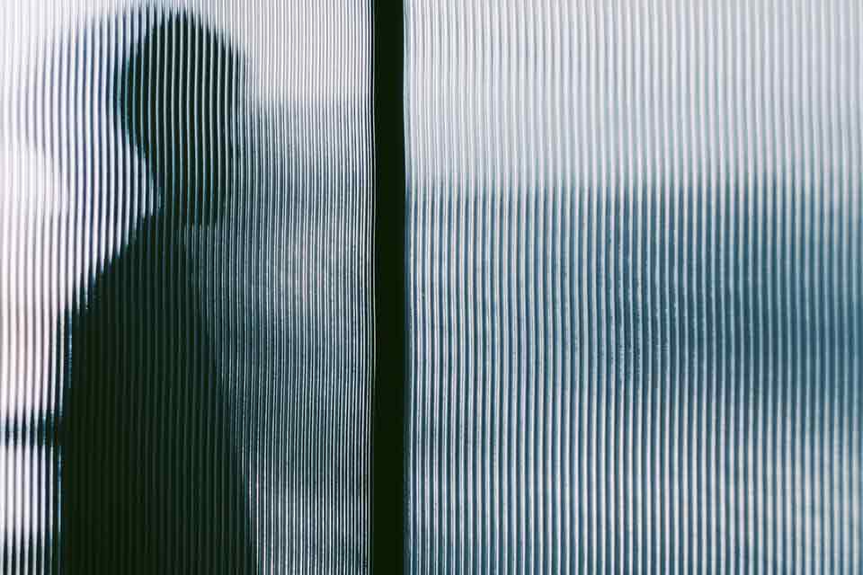 A human figure in silhouette through opaque textured glass