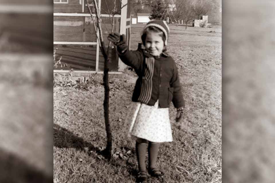 A black and white photograph of a young girl waving at the camera