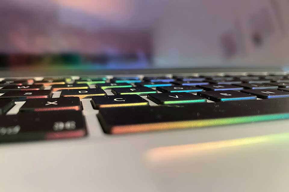 A close-up detail of a computer keyboard that is underlit by rainbow colored LEDs