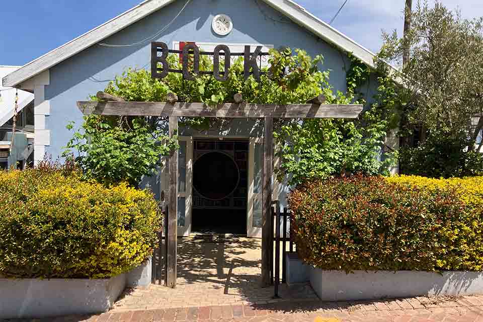 A modest blue home with plants and ivy almost swallowing the entrance