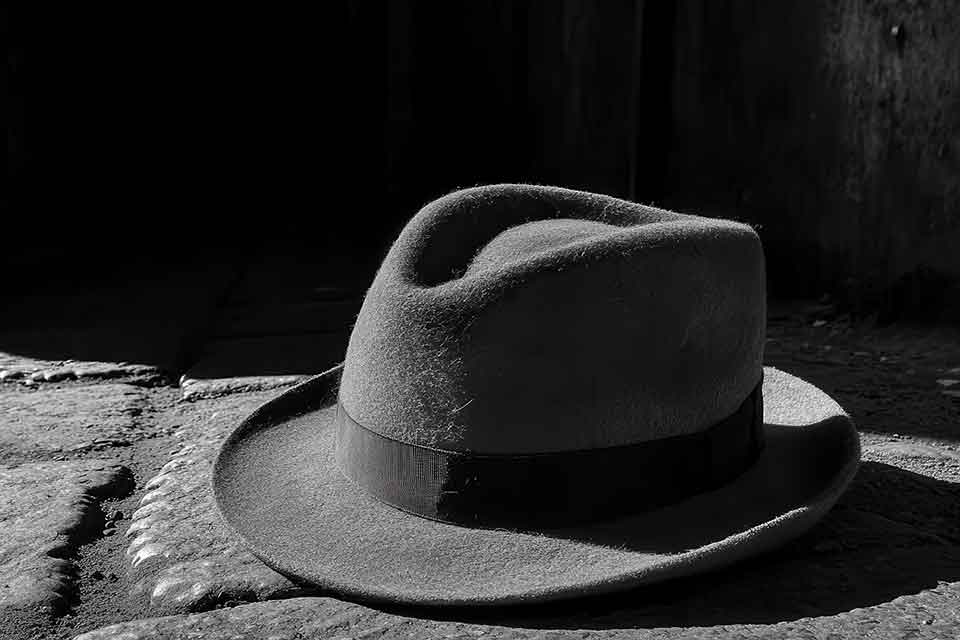 A man's hate sits partially illuminated by sunlight on a table.