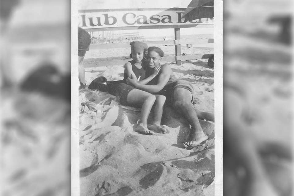 A black and white photo of a man and a woman embracing while they lay in the sand