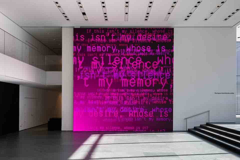 Ghostly electronic words inhabit a dark magenta canvas in a white museum hall
