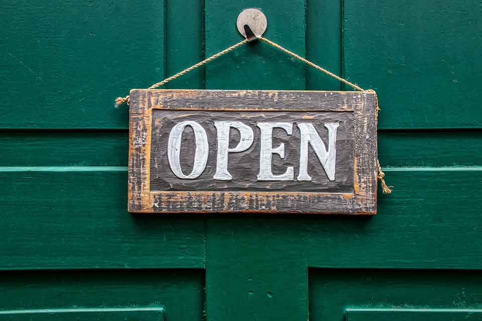 A weather wooden sign that reads, "Open" hanging on a door painted forest green