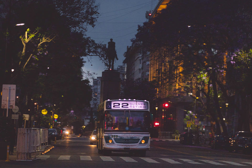 A photograph of a bus traversing a crowded city street at dusk