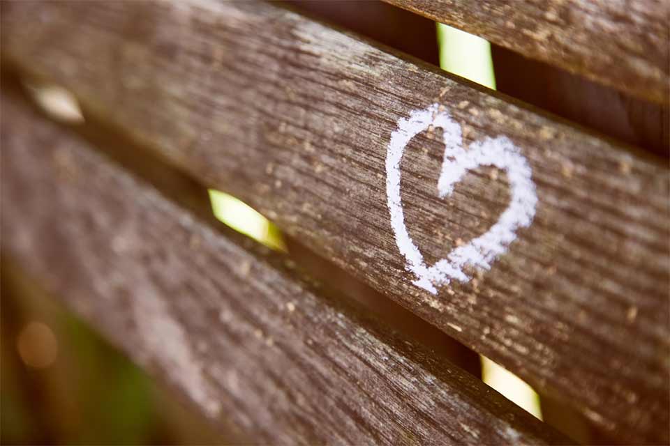 A photograph of a wooden bench with a heart drawn on it in chalk