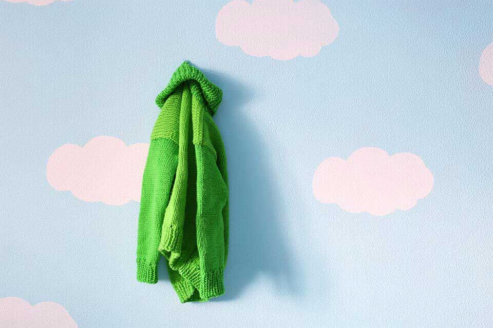 A bright green sweater hanging on a wall painted sky blue with clouds