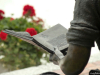 Sculpture of person reading a book in a park with red flowers