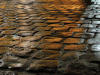 A cobbled street, under street lamps at night, gradating in color from brown to grey.