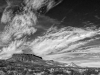 A black and white photograph of a cloud streaked sky above a mesa and the scrublands below